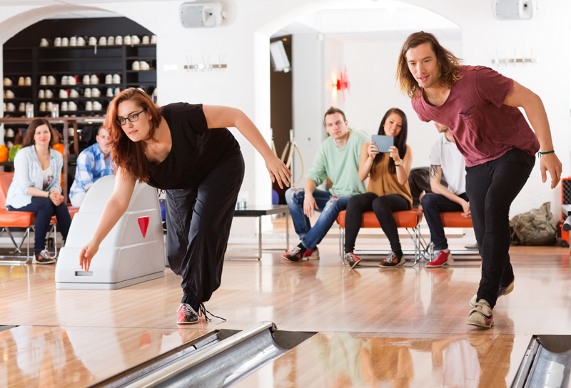 Young man and woman playing in bowling alley with friends in bac